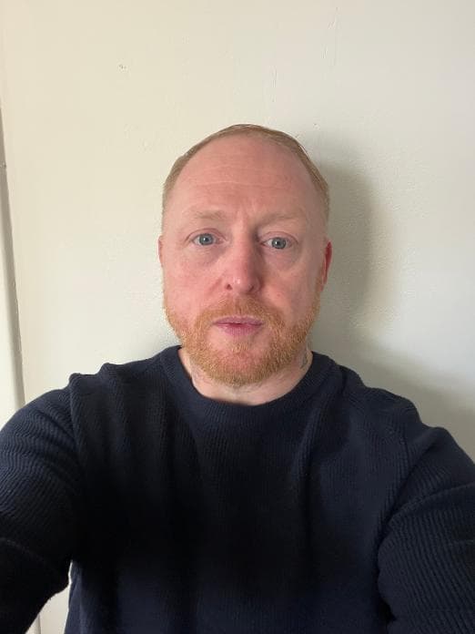 Fair-skinned man with blue eyes and a ginger beard wearing a navy ribbed sweater.